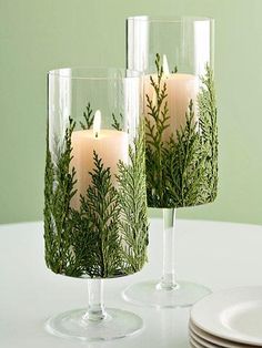 two candles are sitting in glass vases on a table with plates and napkins