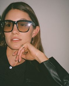 a woman wearing glasses and holding her hand to her face while looking at the camera