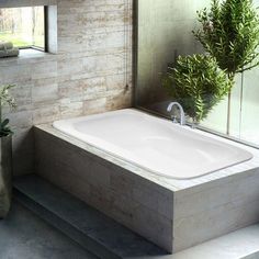 a white bath tub sitting next to a plant in a vase on top of a counter