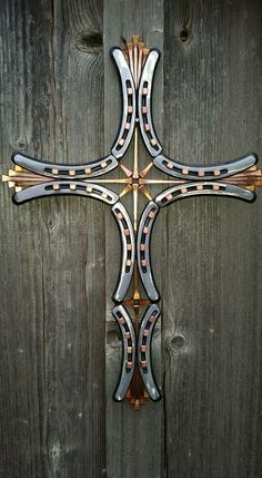 a metal cross mounted to the side of a wooden fence with an intricate design on it