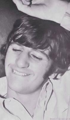 a black and white photo of a young man with his hands on his head, smiling