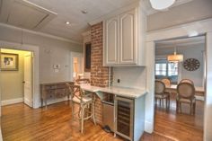 an open kitchen and dining room area with hardwood floors, white cabinets, and brick wall