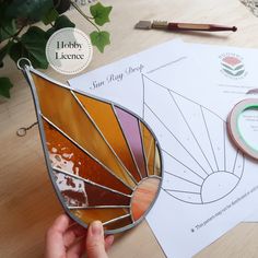 a person holding a stained glass sun catcher next to paper and scissors on a table