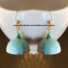 a pair of blue and gold colored earrings on a white plate with light shining through the background