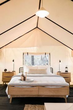 a bed sitting inside of a white tent next to two nightstands and a mirror