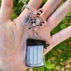 a hand holding a plastic keychain with a trash can and skull on it