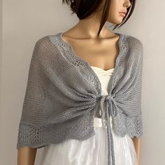 a mannequin wearing a white dress and gray knitted shawl with an open front