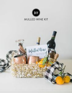 a wine gift basket filled with bottles, glasses and oranges on a white table