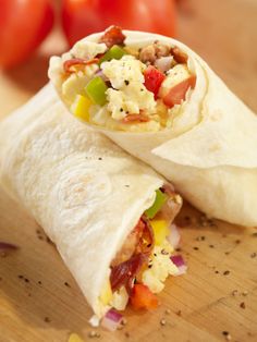 two burritos are on a cutting board with vegetables in the backgroud