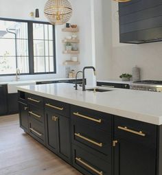 a kitchen with black cabinets and white counter tops, gold pulls on the handles in front of an open window