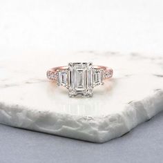 an emerald cut diamond ring with three baguets on top of it, sitting on a marble slab