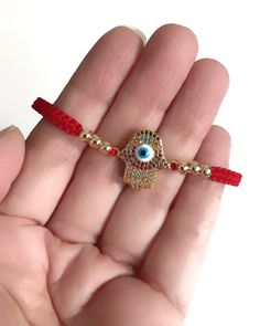 "Gold Evil Eye Bracelet This bracelet is woven with a macrame square knot and a red cotton-linen cord. At the center has a 2 cm cubic zirconia enameled evil eye Hamsa hand 18K gold plated connector decorated with 4mm gold-filled balls on each side. Bracelet minimum size: 6\" or 15 cm and can be extended to 8\" or 20cm approximately. This cute bracelet can be adjusted to a different length if needed. It's a great look for daytime, clean line, fashion, and urban look. Back to the shop: https://www Red Macrame Bracelet Jewelry, Red Macrame Jewelry For Beach, Red Macrame Jewelry As Gift, Red Macrame Beaded Bracelets For Friendship, Red Macrame Jewelry Gift, Red Bohemian Friendship Bracelets With Adjustable Cord, Bohemian Red Friendship Bracelets With Adjustable Cord, Red Bohemian Friendship Bracelet With Adjustable Cord, Red Macrame Braided Bracelets For Friendship