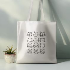 a white tote bag with cats drawn on it next to a potted plant