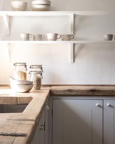 some jars and bowls are sitting on the counter in this white kitchen with wooden counters