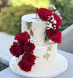 a three tiered white cake with red roses on top and baby's breath