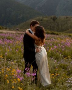 a bride and groom embracing in a field of wildflowers with mountains in the background