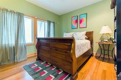 a bed room with a neatly made bed and a rug on the wooden flooring