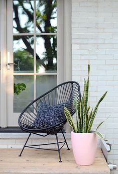 a black wicker chair sitting on top of a wooden porch next to a potted plant