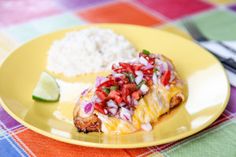 a yellow plate topped with food next to rice and a slice of lime wedges