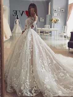 a woman taking a selfie in a wedding dress with flowers on the skirt and long sleeves