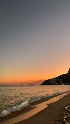 the sun is setting at the beach with waves coming in to shore and mountains in the distance