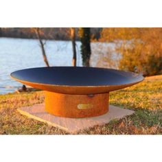 an orange and black fire pit sitting on top of a stone slab in the grass