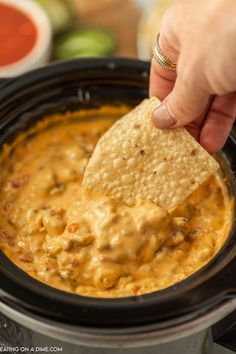 a hand dipping a tortilla chip into a crock pot filled with salsa