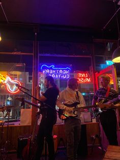 three people are playing instruments in front of a neon sign that reads northern guitar club