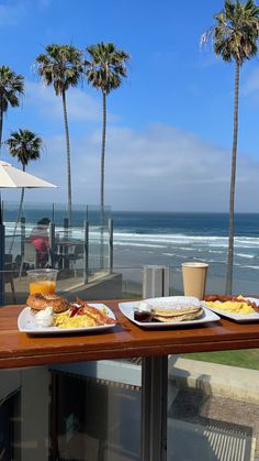 two plates of food sit on a table overlooking the ocean and palm trees in front of them