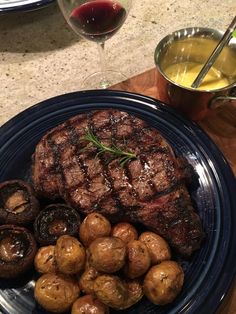 a steak and some potatoes on a plate with a glass of wine next to it