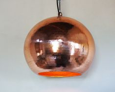 a copper colored light hanging from a hook on a white wall with an orange circle in the center