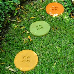 three different colored buttons sitting on top of green grass with the words diy cement button stepping stones