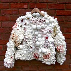 a white jacket hanging on a brick wall next to a wooden hanger with red and white balls all over it