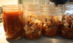 four jars filled with food sitting on top of a counter next to a stovetop