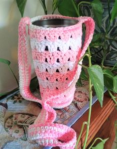 a crocheted pink and white cup on a table next to a potted plant