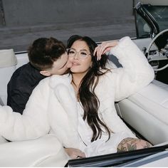 a man and woman sitting in the back of a white convertible car, with their arms around each other