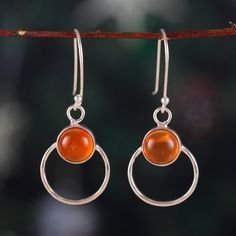 Mysterious and magical, Sapna Mehta's newest design captures the beauty of the universe and combines it with glamour. As an expert in jewelry creations, the designer works with Indian artisans to create these dangle earrings, whose round formations are made from polished sterling silver. The touch of uniqueness is in the warm-toned carnelian stones set at the center, symbolizing courage with their intense light. Elegant Carnelian Earrings, Orange Gemstone Dangle Jewelry, Carnelian Gemstone Dangle Earrings, Amber Carnelian Gemstone Earrings, Amber Gemstone Drop Earrings, Orange Gemstone Dangle Earrings, Orange Sterling Silver Round Jewelry, Carnelian Gemstone Dangle Jewelry, Carnelian Dangle Jewelry With Matching Earrings