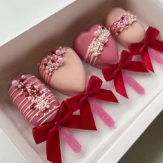 three heart shaped cookies in a box with red ribbon and bows on the top one