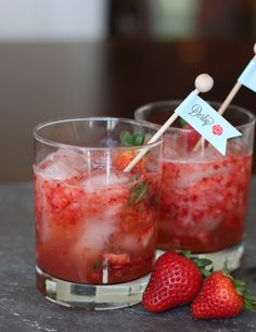 two glasses filled with liquid and strawberries on top of a table next to each other