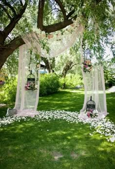 an outdoor ceremony setup with flowers and birdcages on the grass, surrounded by trees