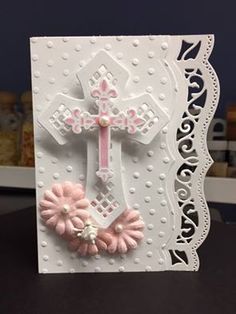 a white card with pink flowers and a cross on the front, sitting on top of a table