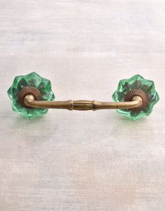 a green glass door handle on a white surface with a gold colored handle and two flowers in the center