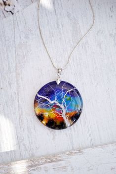 a glass pendant with a tree in the middle on a white surface, hanging from a chain