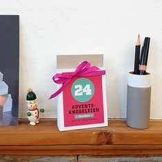 a wooden shelf topped with art supplies and a small box filled with pencils on top of it