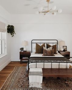 a bedroom with white walls and wood flooring has a black iron bed frame, two nightstands, and a rug on the floor