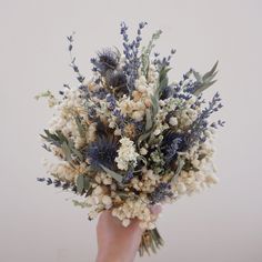 a hand holding a bouquet of flowers with blue and white blooms in it's center