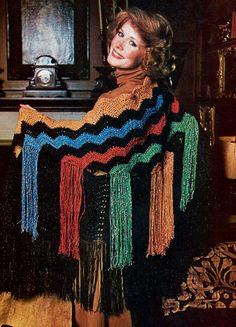 a woman sitting in a chair wearing a crocheted shawl with fringes