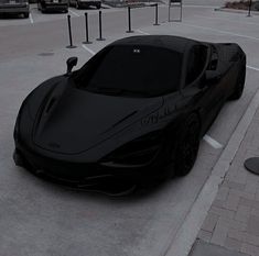 a black sports car parked in a parking lot next to a sidewalk with cars on it