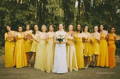 a group of women standing next to each other in front of trees and bushes, all wearing yellow dresses