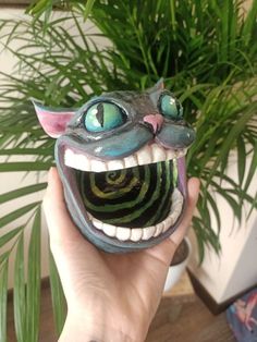 a hand holding up a fake toothy monster head with green eyes and mouth wide open